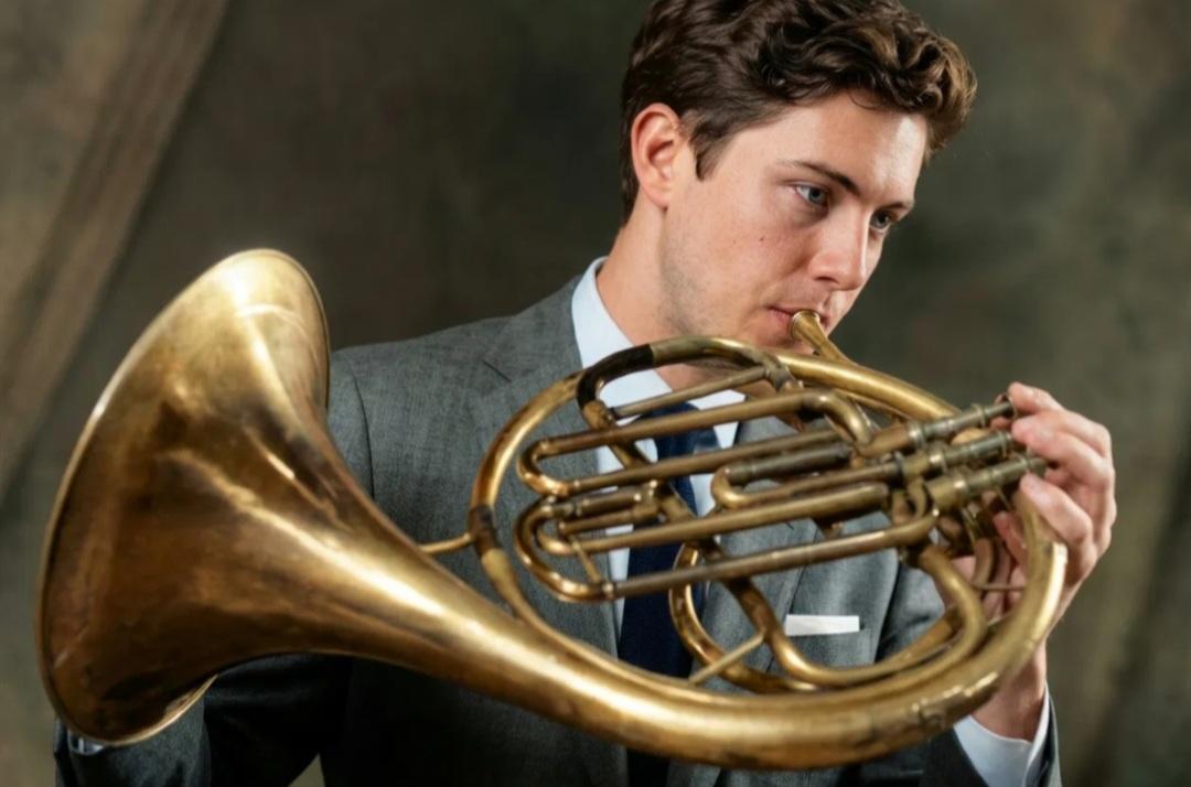 Trevor Nuckols playing horn in a grey jacket