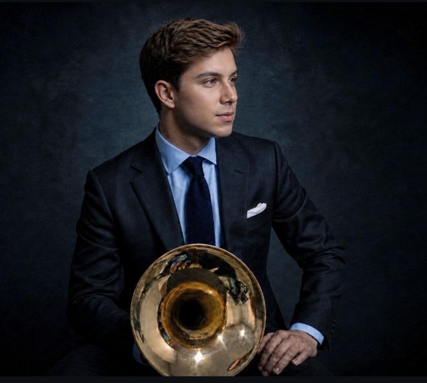 Trevor Nuckols in a navy suit holding a horn bell