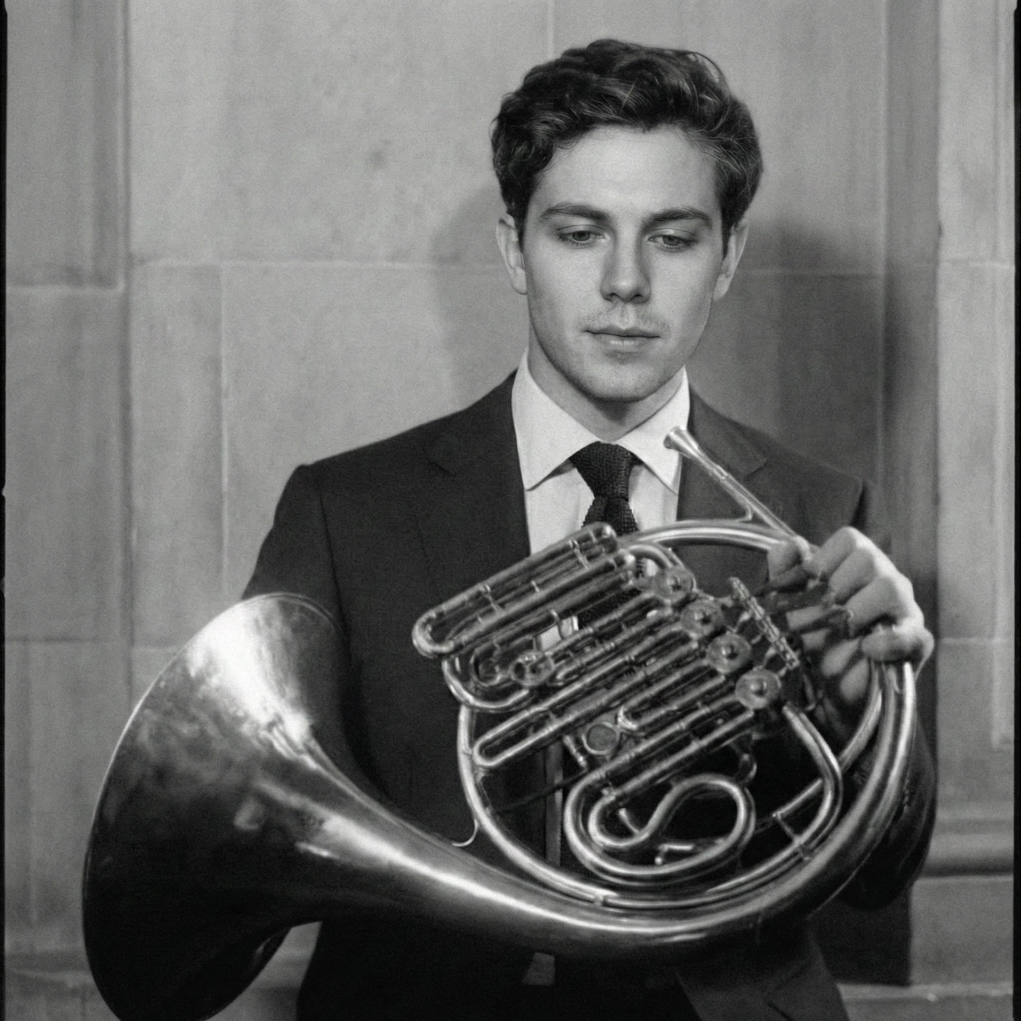 Black and white portrait holding horn against stone wall