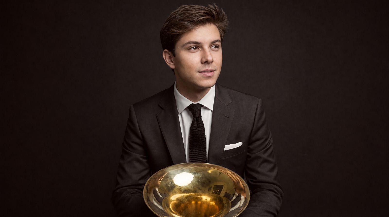 Trevor in charcoal suit holding a horn bell