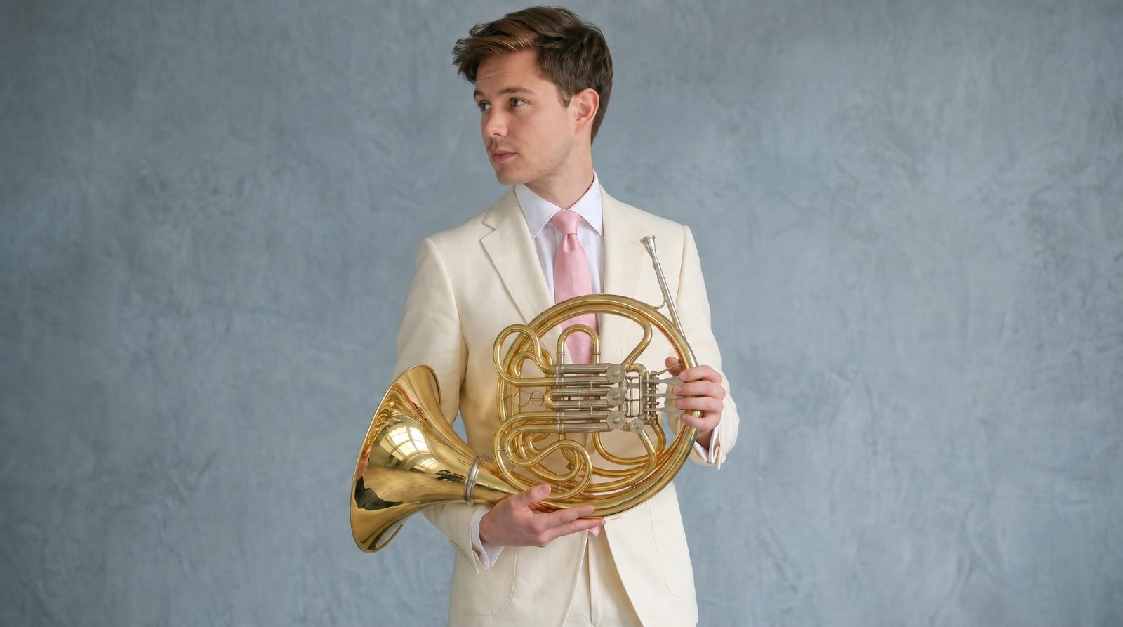 Trevor Nuckols in a cream suit holding a French horn